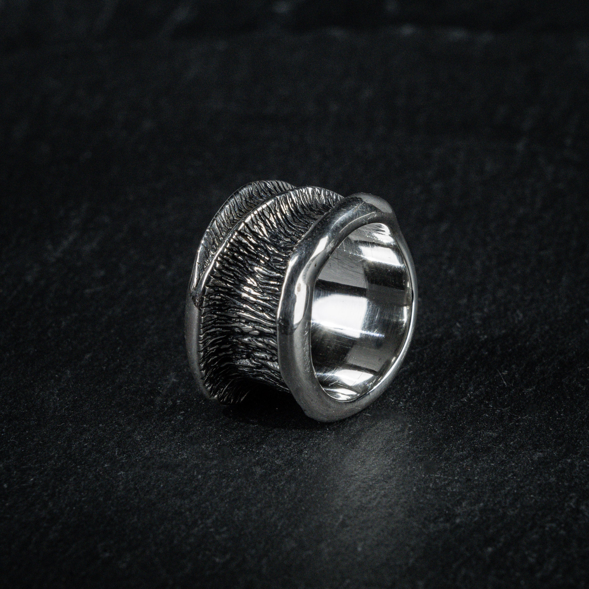 Statement ring 'Talon' by Myon Rox – curved silhouette and waterfall-inspired texture, standing on slate