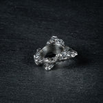 oxidized silver ring with a textured, rugged surface resembling volcanic ash, with a slightly uneven finish, displayed on a dark, textured background.