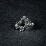 oxidized silver ring with a textured, rugged surface resembling volcanic ash, with a slightly uneven finish, displayed on a dark, textured background.