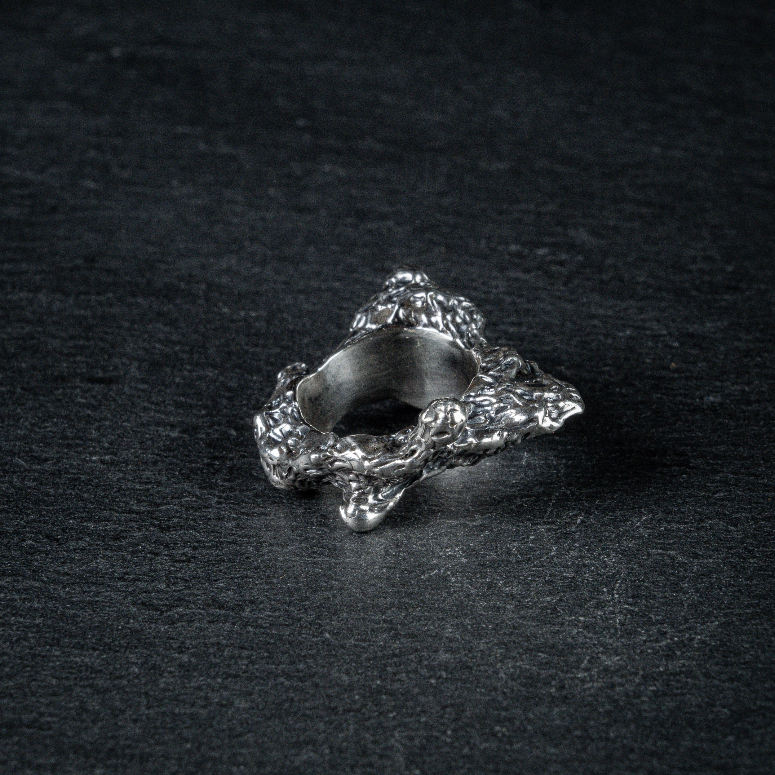 oxidized silver ring with a textured, rugged surface resembling volcanic ash, with a slightly uneven finish, displayed on a dark, textured background.