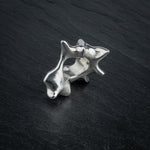 SYRINX organic massive silver sculptural statement ring standing on dark slate, side view