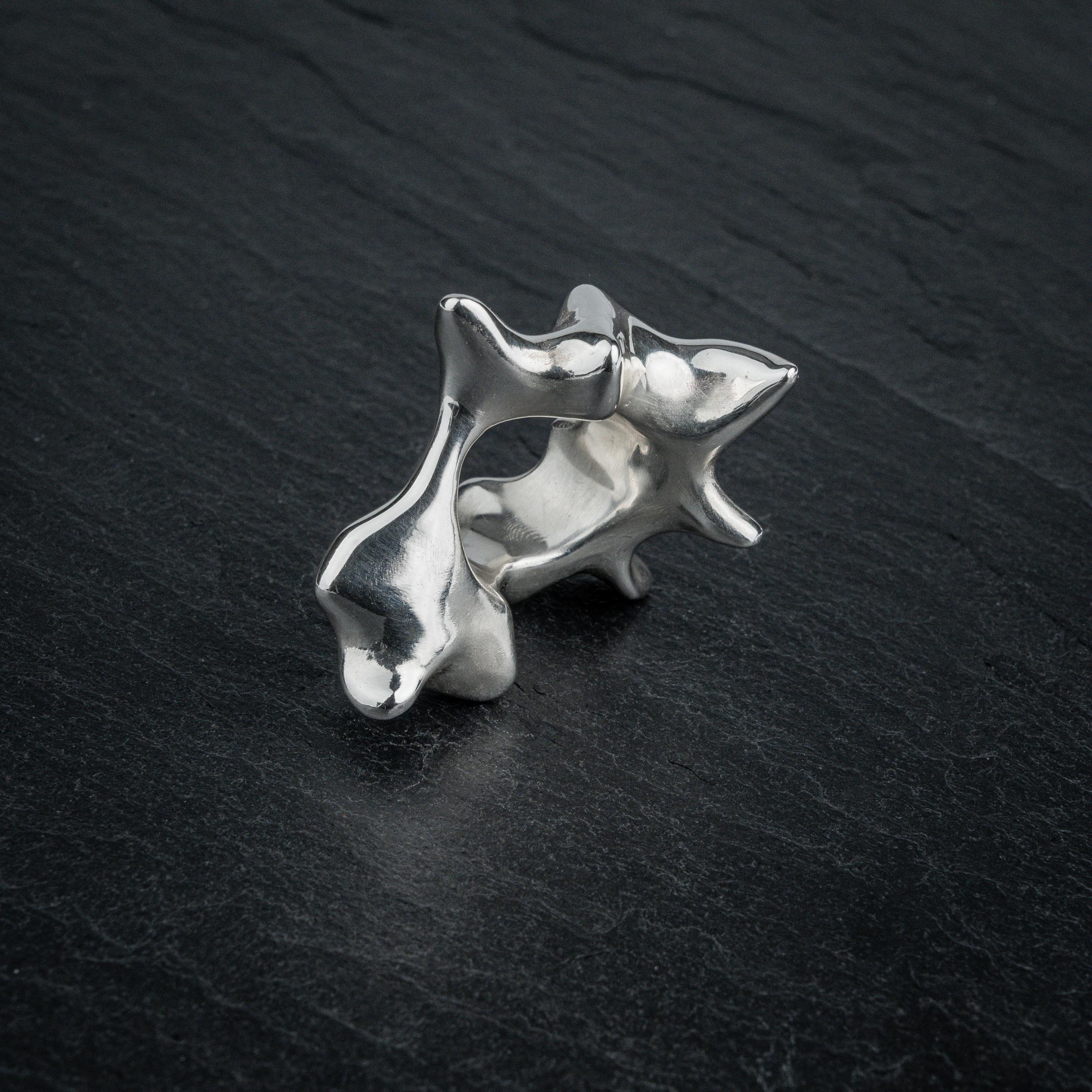 SYRINX organic massive silver sculptural statement ring standing on dark slate, side view