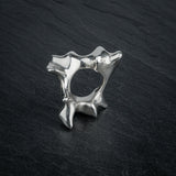 SYRINX organic massive silver sculptural statement ring standing on dark slate, view through ring