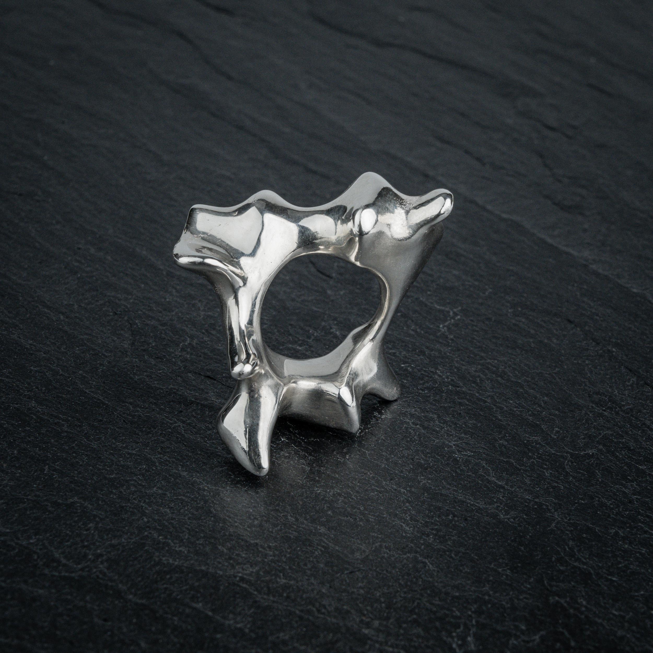 SYRINX organic massive silver sculptural statement ring standing on dark slate, view through ring