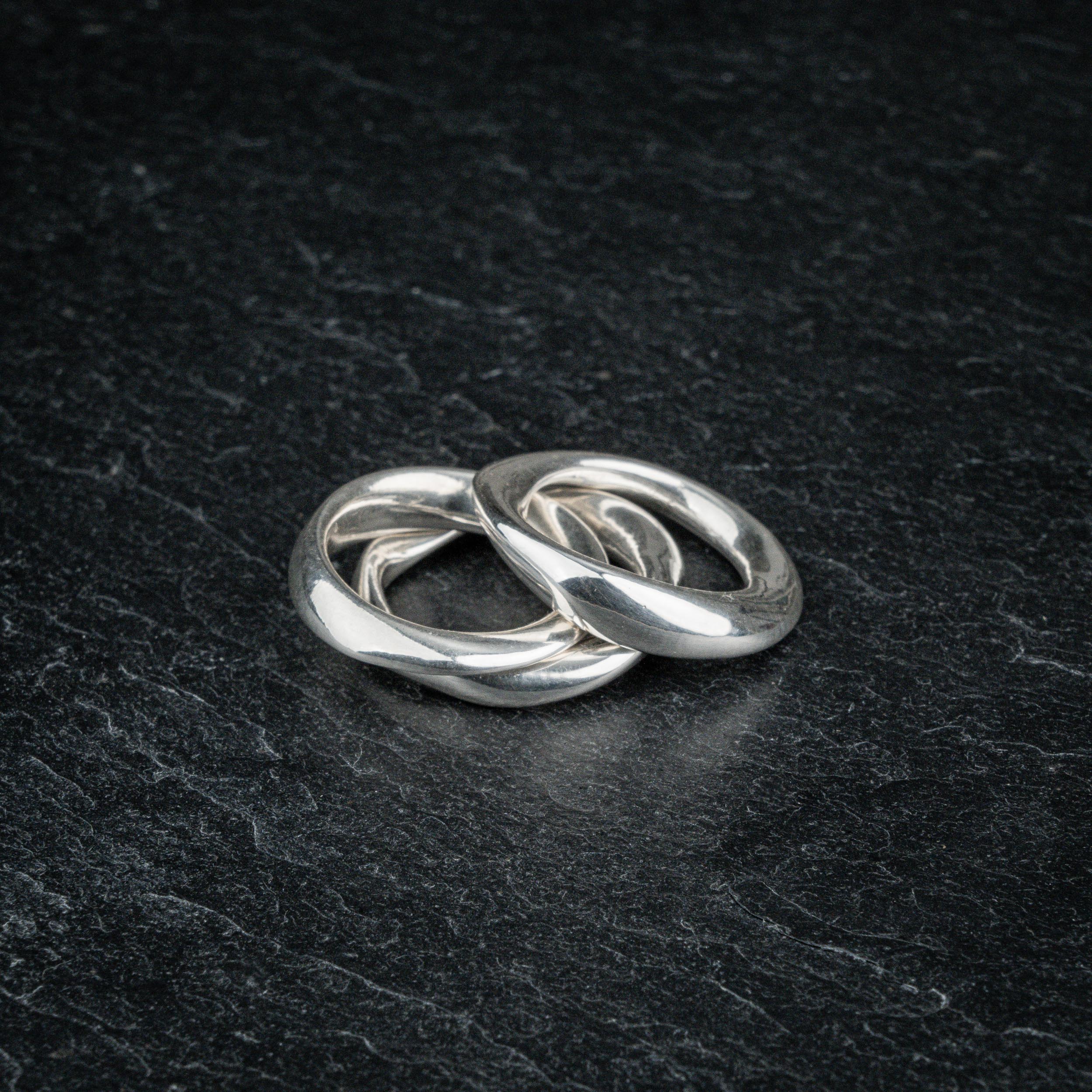 TRI_M three stackable silver Möbius strip rings partially overlapping on slate