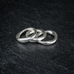 TRI_M three stackable silver Möbius strip rings overlapping each other on slate