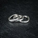 TRI_M three stackable silver Möbius strip rings overlapping each other on slate