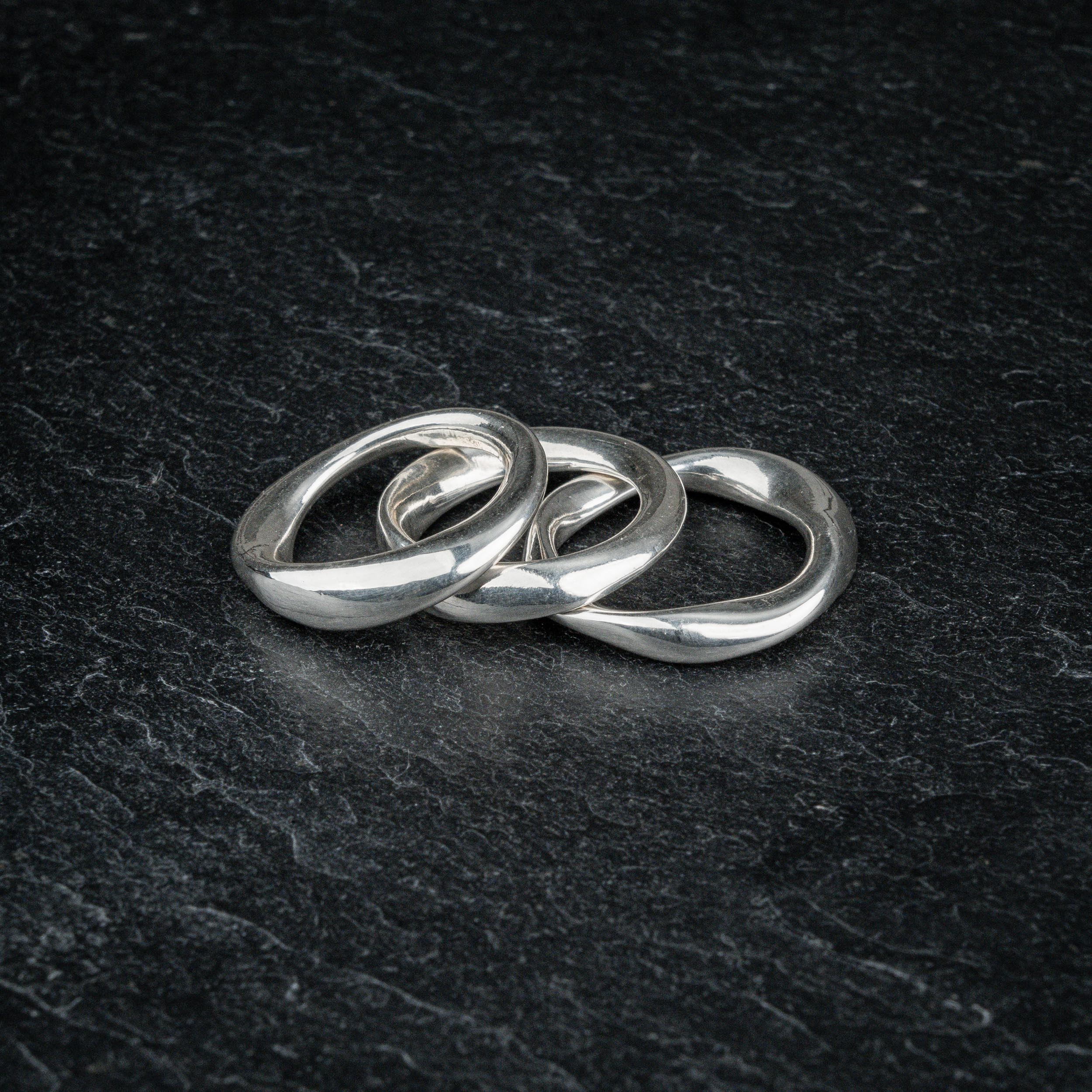 TRI_M three stackable silver Möbius strip rings overlapping each other on slate