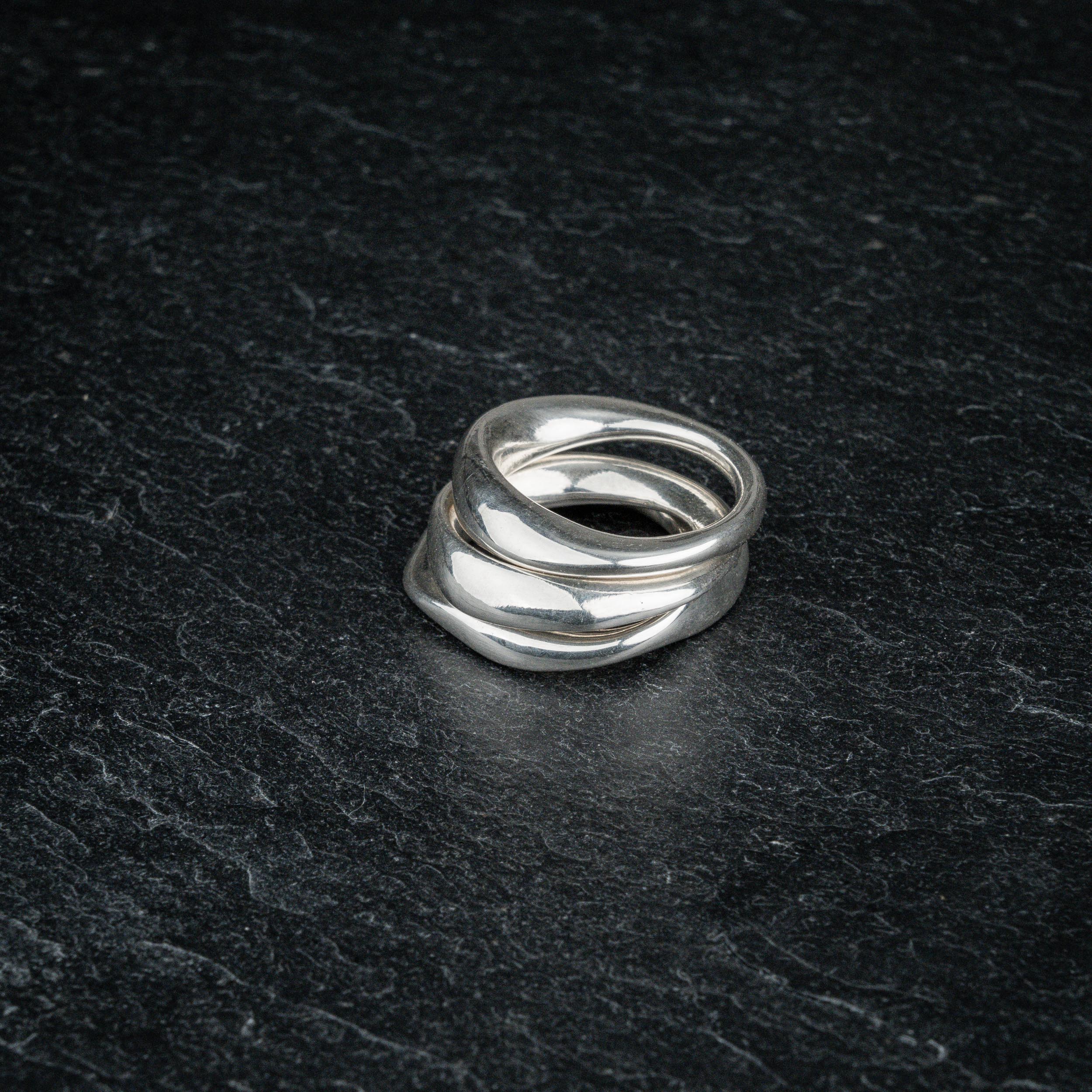 TRI_M three stackable silver Möbius strip rings stacked on top of each other on slate