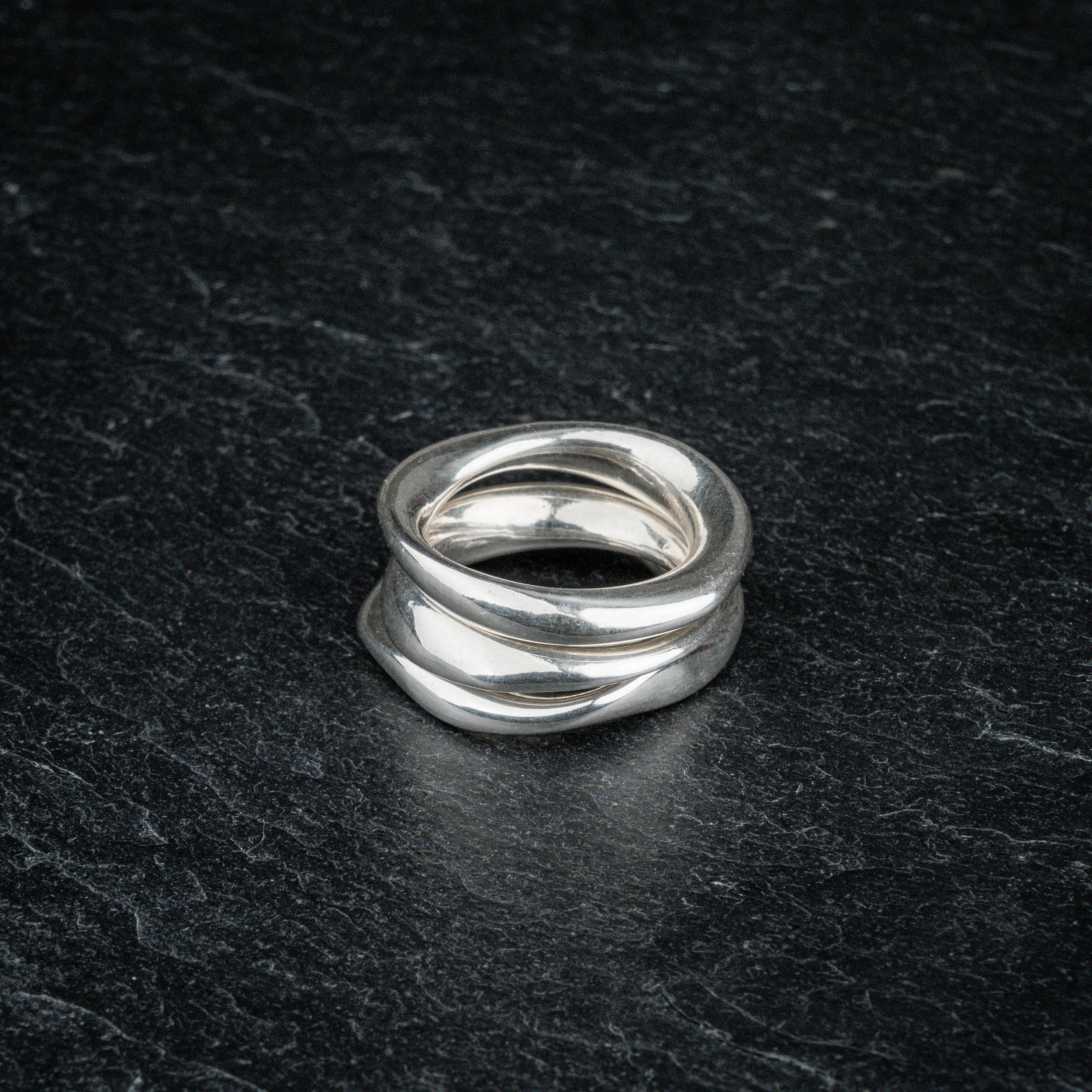 TRI_M three stackable silver Möbius strip rings layered on top of each other on slate